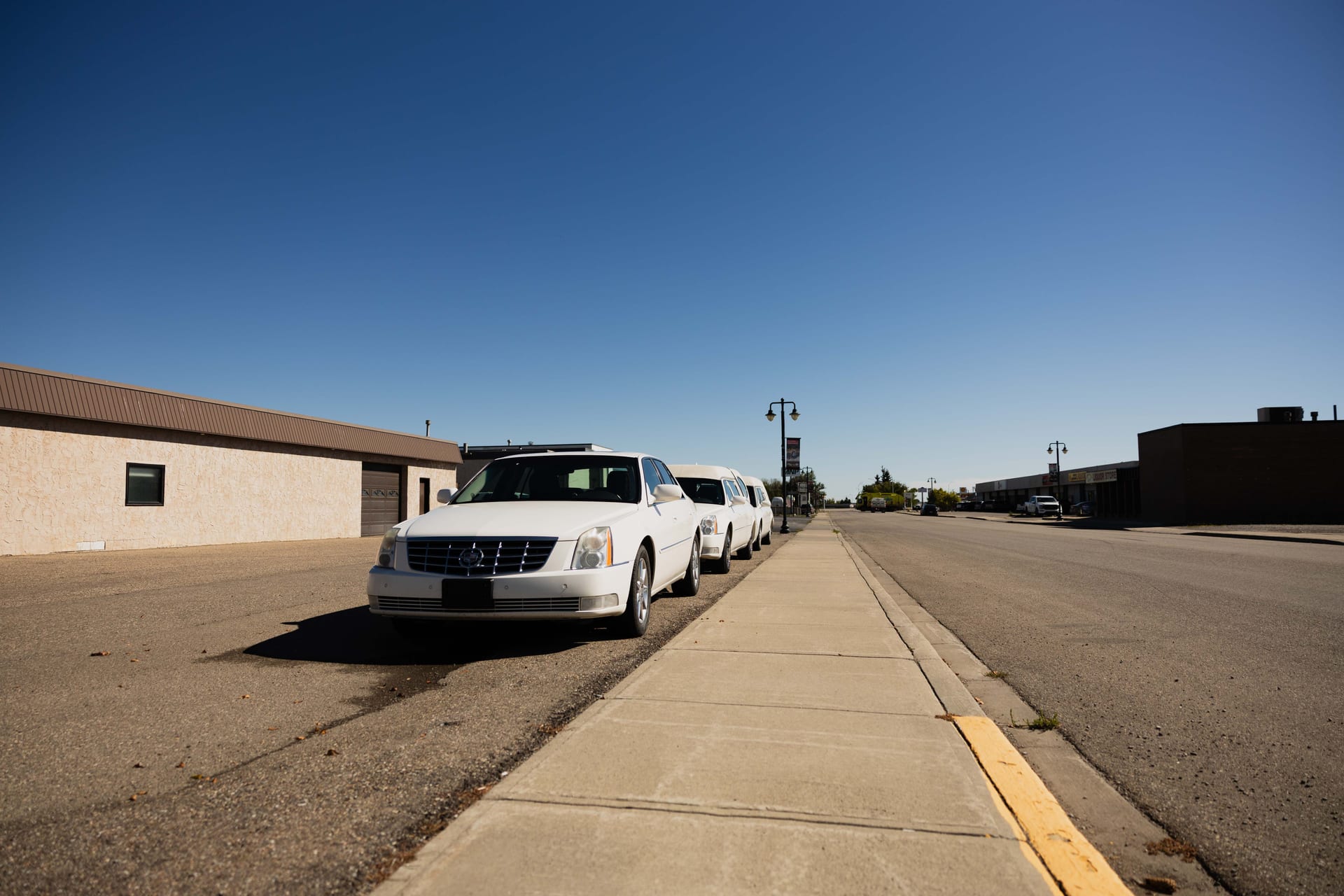 Looking down 5th Avenue in Fort Macleod past Eden's Funeral Home, a white limousine and funeral coach parked at the kerb