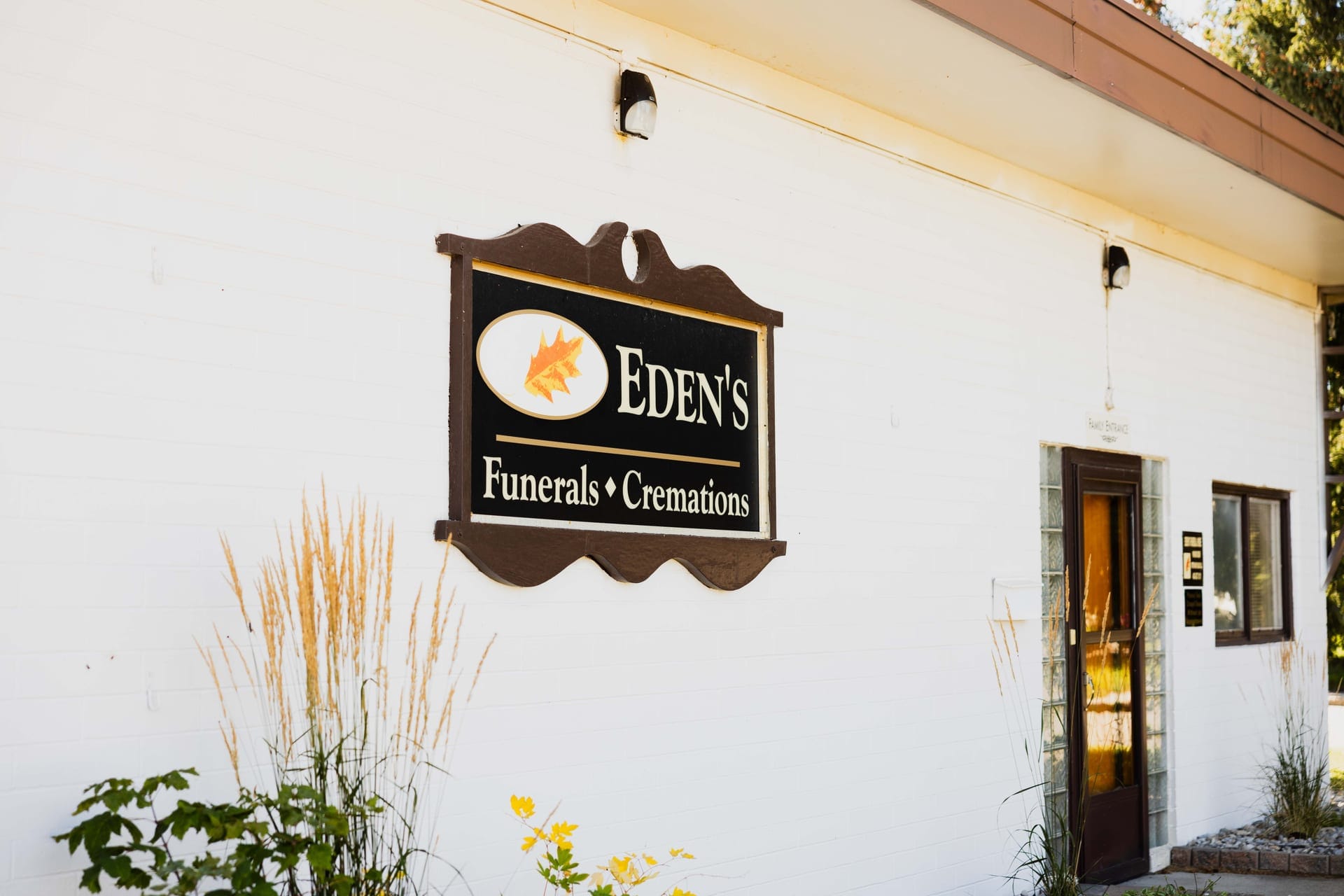 The oval Eden's Funerals & Cremations sign on the white brick wall of the Pincher Creek funeral home, beside the front door